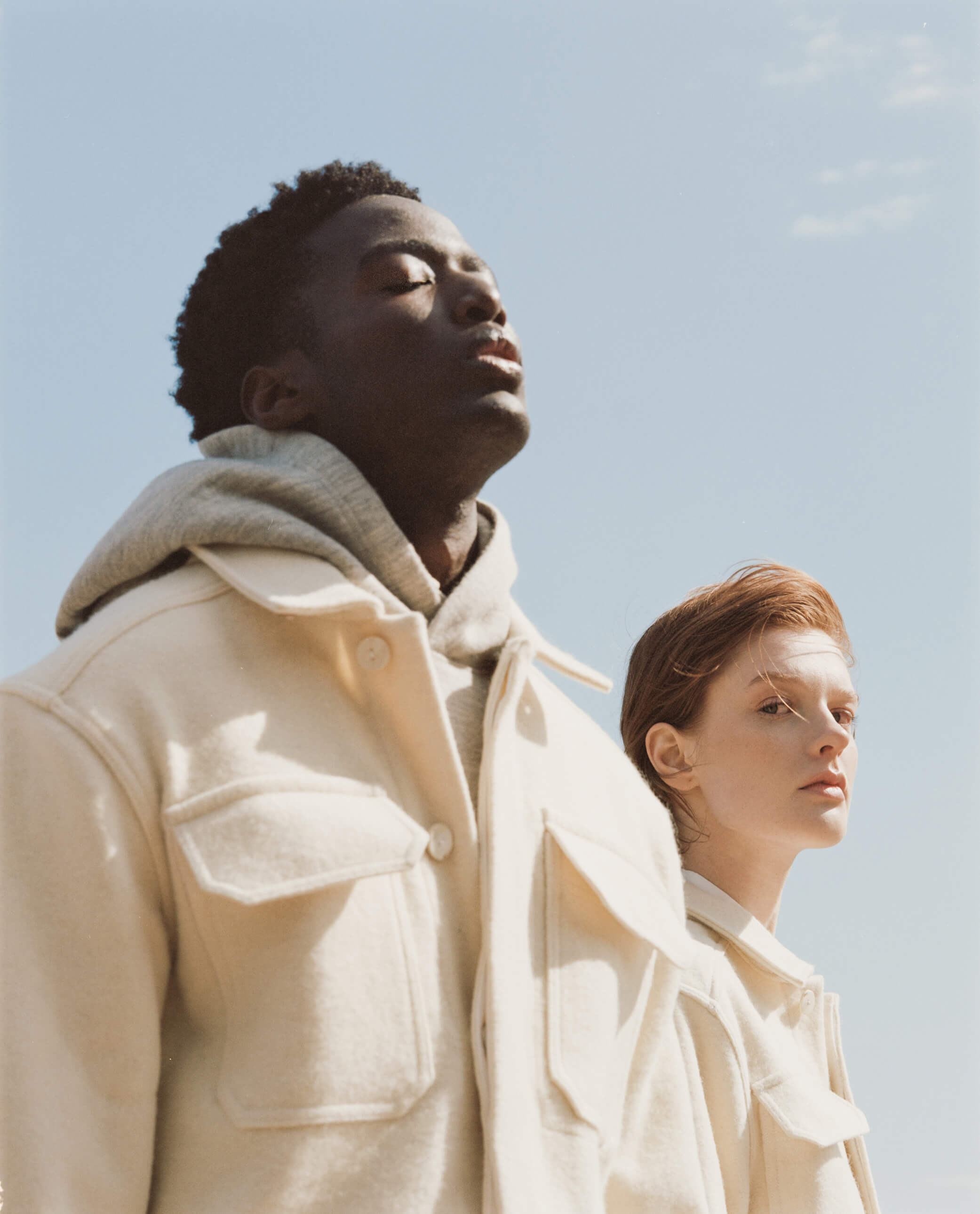 A man and a woman are wearing undyed wool jackets. The man is looking up at the sky. The woman looks at the camera.
